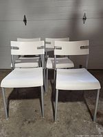 Front view of four white IKEA Laver stacking chairs with gray metal legs and plastic seats and backs. Shows design and condition.