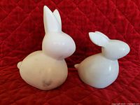 Photo showing front and side of large and small white marble bunny figurines on red quilted backdrop.