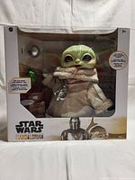Front view of boxed Star Wars The Mandalorian The Child plush with visible accessories.