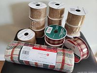 Thirteen rolls of assorted wired ribbon including stacks of burlap ribbon and plaid wired ribbon with spools for each roll visible.