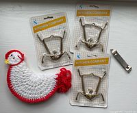 Group photo of three unopened plate hanger packages, crocheted chicken handle protector, and Ecko can piercer