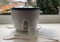 Front view of homeMAX rice cooker with lid, accessories and manual displayed