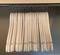 Front view of twenty-two white wooden hangers on closet rod
