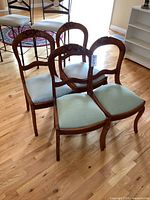 Four antique solid wood chairs with upholstery, two with light blue-green fabric and two with light striped fabric, arranged together on a hardwood floor.