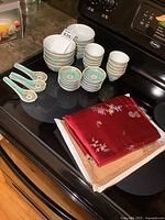 Full set of porcelain bowls in three sizes along with matching spoons and folded silk-like fabric