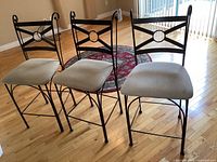 Three metal framed bar height chairs in a row showing fabric seat differences and black metal frame with decorative backrest.