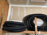 Photo showing two large black coils of ribbed Big O pipe on a wooden shelf in a garage setting.