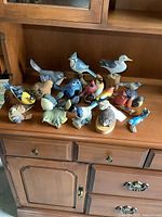 Overall photo of collection on wood cabinet showing variety of painted wood and resin bird figurines along with hedgehog figurine.