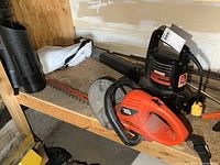 Overview of Black & Decker hedge trimmer with Orange Hog blade and Craftsman electric leaf blower on workbench surface.