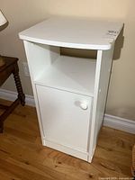 Front view of white melamine cabinet with single door and open shelf, showing minor wear on top and sides.