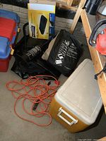 Wide shot showing Coleman cooler, air pump, extension cord, and air beds in storage bags on the floor.