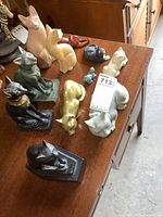 All eleven cat figurines arranged on wooden furniture surface. Materials include porcelain, wood, brass, and resin.