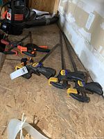 Six clamps consisting of three large Irwin Quick-Grip bar clamps and three smaller clamps arranged on the floor.