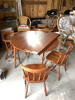 Solid maple oval dining table surrounded by four spindle-back chairs, shown with one leaf partially on table.