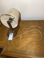 Wooden lamp with cord, base and turned stem, shade visibly stained and frayed.