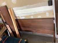 Walnut wood headboard resting against a wall in a garage, showing wood grain and polished surface.