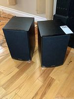 Pair of black Energy Connoisseur CB-20 bookshelf speakers standing on wooden floor with fabric grills covering the front, showing brand logo.