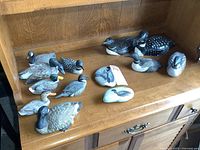 Bird figurines displayed on wooden surface, mix of wood, resin, stone materials, multiple species depicted