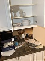 Photo of kitchen counter and shelves showing various dishes, glassware, candles, and linens