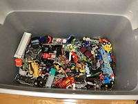 Photo showing large bin filled with multiple small diecast toy vehicles including cars, trucks and construction vehicles in various colors