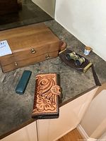 Wooden jewelry box, tooled leather wallet, green case with buttons, and mother of pearl opera glasses on counter