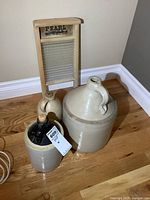 Photo showing three vintage stoneware jugs of varying sizes and a wooden washboard with metal scrubbing surface.