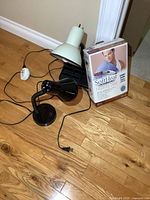 Two desk lamps, one black flexible-neck and one white with storage base, alongside boxed SoftHeat heating pad.