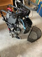 Two folding mobility carts side by side on concrete floor, one with detached wire basket on floor