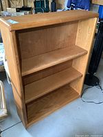 Full frontal view of oak bookcase showing 3 shelves with 2 adjustable shelves visible and wooden back panel.