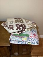 Two folded old patchwork quilts stacked on a wooden cabinet, showing part of the colorful patchwork pattern and the cross pattern quilt.