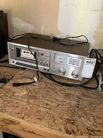 Full front view of vintage Sanyo cassette deck with cassette inserted, power cord visible, placed on wooden surface.