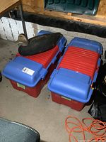 Photo showing two red Rubbermaid storage totes with blue lids stacked side by side, black vintage cork duck decoy placed on top of one tote.