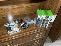 Photo shows 12 Xbox and Xbox 360 game cases and game discs on wooden furniture
