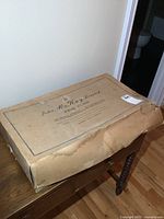 Closed vintage McKay Furs branded cardboard box showing wear and tear, storing the race car set.