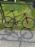 Side view of the men's Kona Fire mountain bike showing maroon frame and red front suspension fork along with knobby tires.