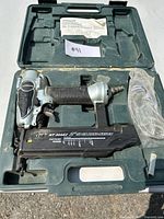 Full view of Hitachi brad nailer in molded plastic case with instruction manual and an accessory wrapped in plastic.