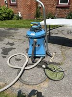 Blue industrial wet and dry vacuum cleaner with hoses and attachments on asphalt, outdoor setting.