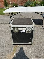Front view of locking wheeled stage box showing black textured surface with reinforced metal protective corners and two latch locks.