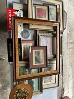 Photo showing the lot of assorted framed prints, wooden frames, signs, and a carved tribal mask laid out on a surface.