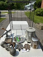 Overall display of miscellaneous lot items including wire rack, trash cans, metal trivets, ashtray, bottle openers and other small kitchen household items