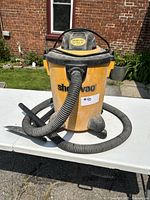 Front view of yellow and black Shop Vac wet/dry vacuum with hose attached, showing general shape and condition