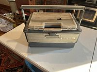 Closed dark gray and off-white Tackle Locker fishing tackle box with handle and two latches on the lid.