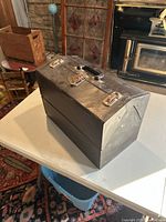 Closed large metal tackle box with handle and metal clasps on a table.