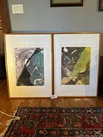 Two large framed abstract prints leaning against a wall showing differing abstract compositions with emphasis on greens and yellows