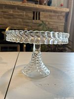 Side profile of a clear glass cake stand showing textured leaf pattern and bubble design base
