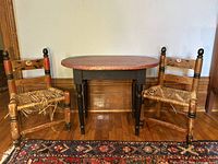 Full view of the set with the oval children's table and two Folk Art style chairs showing woven rush seats needing repair.