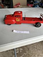Side view of red vintage Lincoln fire truck toy showing cab and flatbed rear with decals.