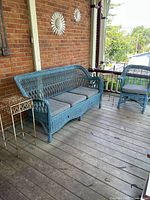 Wide shot of porch showing blue wicker sofa, matching chair, and one metal side table