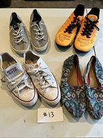 All four pairs of shoes displayed on light-colored surface. Converse All Star white canvas shoes show dirt. Toms patterned slip-ons, Reebok bright orange running shoes, Sperry grey suede slip-ons with white laces.