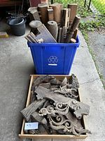 Blue recycling bin filled with carved wooden architectural salvage pieces and a wooden tray with assorted smaller carved wood elements showing scrollwork and floral motifs.
